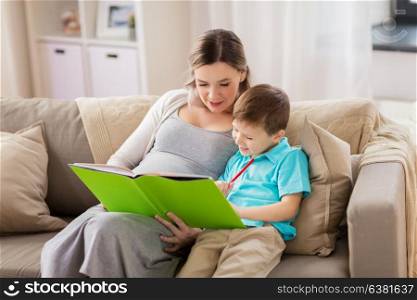 family, education and pregnancy concept - happy pregnant mother and little son with book and pencil at home. pregnant mother and little son with book at home