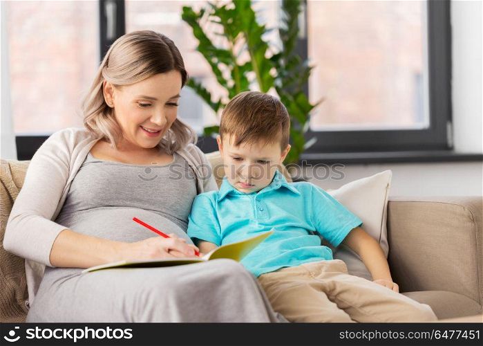 family, education and pregnancy concept - happy pregnant mother with little son writing or drawing in workbook at home. pregnant mother with workbook and son at home. pregnant mother with workbook and son at home