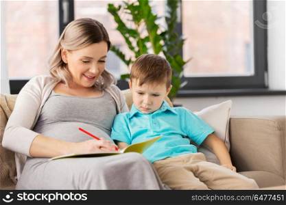 family, education and pregnancy concept - happy pregnant mother with little son writing or drawing in workbook at home. pregnant mother with workbook and son at home. pregnant mother with workbook and son at home