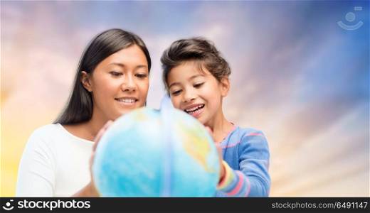 family, education, travel and people concept - mother and daughter with globe over evening sky background. happy mother and daughter with globe over sky. happy mother and daughter with globe over sky