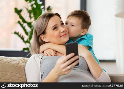 family, emotions and pregnancy concept - little son kissing happy pregnant mother with smartphone at home. son kissing happy pregnant mother at home. son kissing happy pregnant mother at home