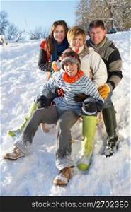 Family Enjoying Sledging Down Snowy Hill