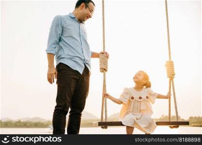 Family enjoying their vacation in nature, with the children playing on a swing set in a beautiful garden at sunset, while the parents sit and watch feeling the love and happiness of being together