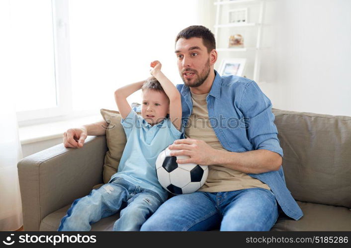 family, entertainment, sport and people concept - father and little son with ball watching football or soccer game tv at home. father and son watching soccer on tv at home