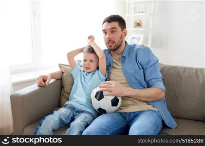 family, entertainment, sport and people concept - father and little son with ball watching football or soccer game tv at home. father and son watching soccer on tv at home