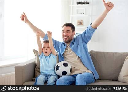 family, entertainment, sport and people concept - happy father and little son with ball watching football or soccer game tv at home. father and son watching soccer on tv at home