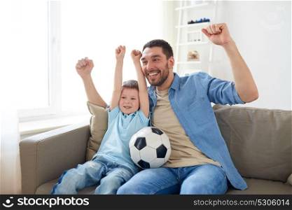 family, entertainment, sport and people concept - happy father and little son with ball watching football or soccer game tv at home. father and son watching soccer on tv at home