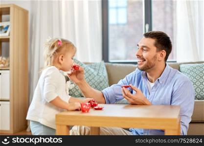 family, fatherhood and childhood concept - happy father and little daughter with toy crockery playing tea party at home. father and daughter playing tea party at home