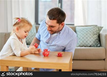 family, fatherhood and childhood concept - happy father and little daughter with toy crockery playing tea party at home. father and daughter playing tea party at home