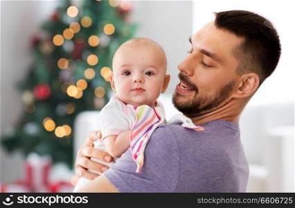 family, fatherhood and holidays concept - father with little baby daughter over christmas tree lights on background. father with baby daughter over christmas tree