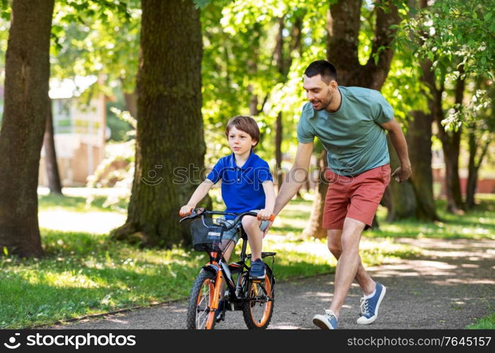 family, fatherhood and leisure concept - happy father teaching little son to ride bicycle at park. father teaching little son to ride bicycle at park