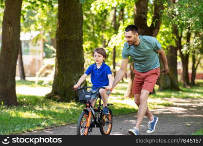 family, fatherhood and leisure concept - happy father teaching little son to ride bicycle at park. father teaching little son to ride bicycle at park