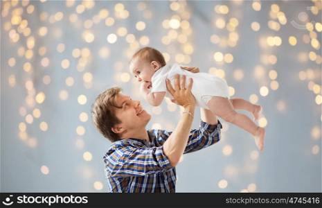 family, fatherhood and parenthood concept - happy smiling young father with little baby over holidays lights background