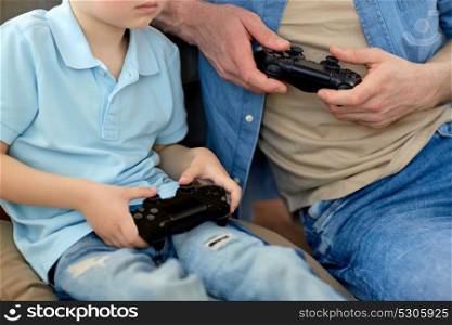 family, fatherhood and people concept - close up of father and little son with gamepads playing video game at home. close up of father and son playing video game