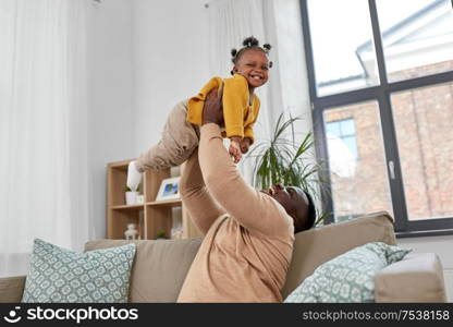 family, fatherhood and people concept - happy african american father playing with baby daughter at home. happy african american father with baby at home