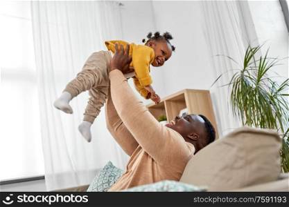 family, fatherhood and people concept - happy african american father playing with baby daughter at home. happy african american father with baby at home