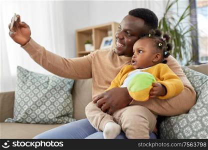family, fatherhood and people concept - happy african american father with little baby daughter taking selfie by smartphone at home. happy father with baby taking selfie at home