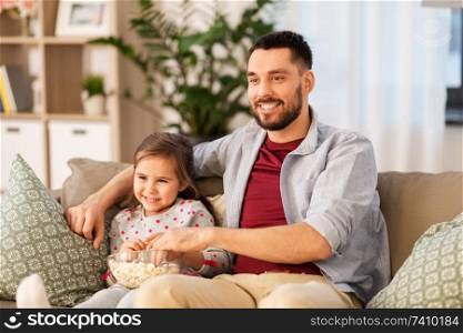 family, fatherhood and people concept - happy father and daughter with popcorn watching tv at home. happy father and daughter watching tv at home