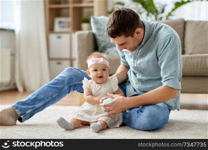 family, fatherhood and people concept - happy father and little baby daughter playing with ball at home. father and little baby daughter with ball at home