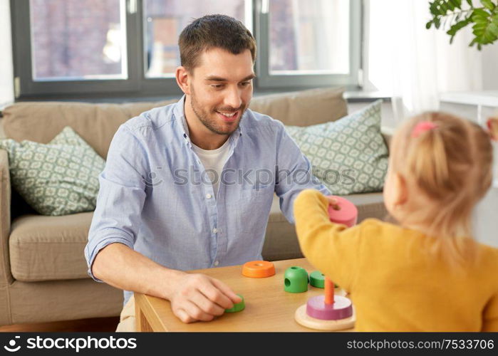 family, fatherhood and people concept - happy father and little baby daughter playing with pyramid toy at home. father playing with little baby daughter at home