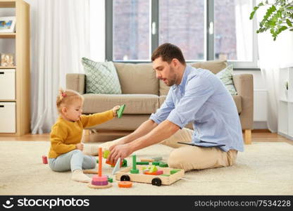 family, fatherhood and people concept - happy father and little baby daughter playing with wooden toy toy blocks kit at home. father playing with little baby daughter at home