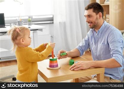 family, fatherhood and people concept - happy father and little baby daughter playing with pyramid toy at home. father playing with little baby daughter at home