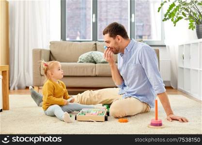 family, fatherhood and people concept - happy father and little baby daughter playing with wooden toy toy blocks kit at home. father playing with little baby daughter at home