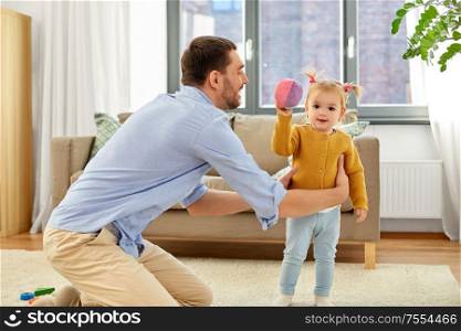 family, fatherhood and people concept - happy father and little baby daughter playing with ball at home. father and baby daughter playing with ball at home