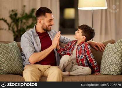 family, fatherhood and people concept - happy father and little son making high five at home in evening. father and son making high five at home in evening