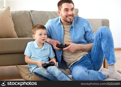 family, fatherhood and people concept - happy father and little son with gamepads playing video game at home. father and son playing video game at home
