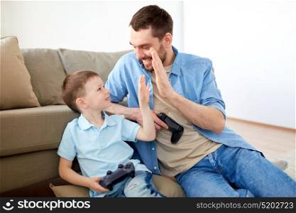 family, fatherhood and people concept - happy father and little son with gamepads playing video game and doing high five at home. father and son with gamepads doing high five