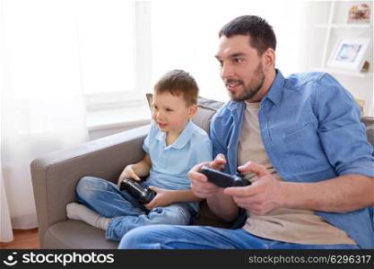 family, fatherhood and people concept - happy father and little son with gamepads playing video game at home. father and son playing video game at home