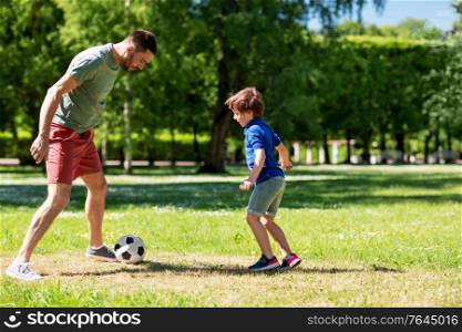 family, fatherhood and people concept - happy father and little son with ball playing soccer at summer park. father with little son playing soccer at park