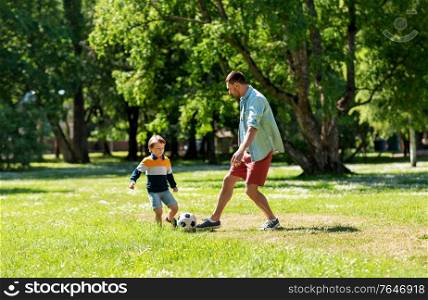 family, fatherhood and people concept - happy father and little son with ball playing soccer at summer park. father with little son playing soccer at park