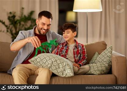 family, fatherhood and people concept - happy father and son playing with toy dinosaur at home in evening. father and son playing with toy dinosaur at home