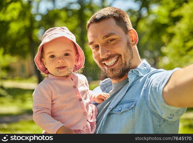 family, fatherhood and people concept - happy father taking selfie with baby daughter at summer park. happy father taking selfie with baby daughter