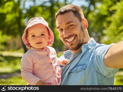 family, fatherhood and people concept - happy father taking selfie with baby daughter at summer park. happy father taking selfie with baby daughter