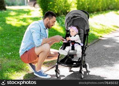 family, fatherhood and people concept - happy father with child in stroller at summer park. happy father with child in stroller at summer park