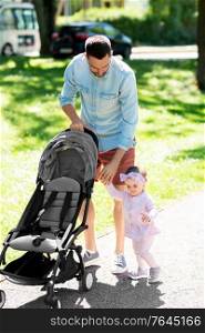 family, fatherhood and people concept - happy father with child or baby daughter and stroller walking at summer park and helping to make first steps. father with child and stroller walking at park