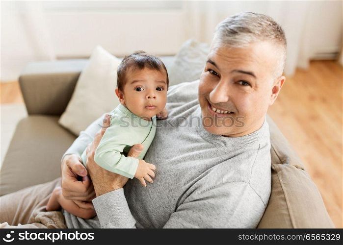 family, fatherhood and people concept - happy father with little baby boy sitting on sofa at home. happy father with little baby boy at home