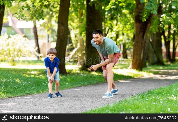 family, fatherhood and people concept - happy father with little son compete in running at summer park. happy father and son compete in running at park