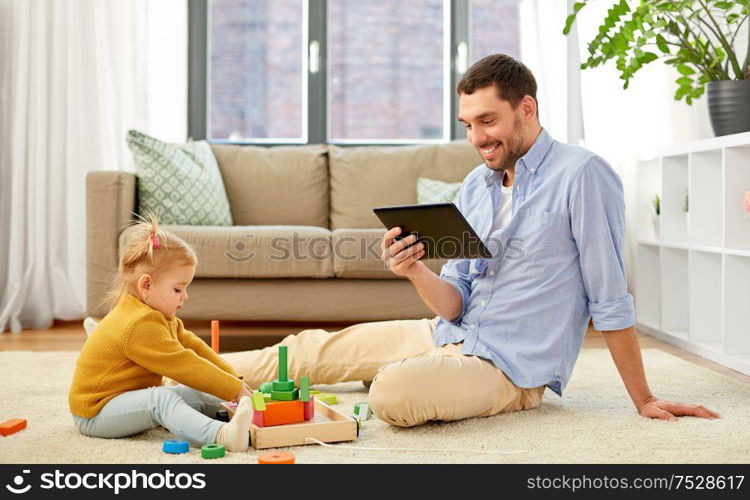 family, fatherhood and people concept - happy father with tablet pc computer and little baby daughter playing with wooden toy toy blocks kit at home. father with tablet pc and baby daughter at home