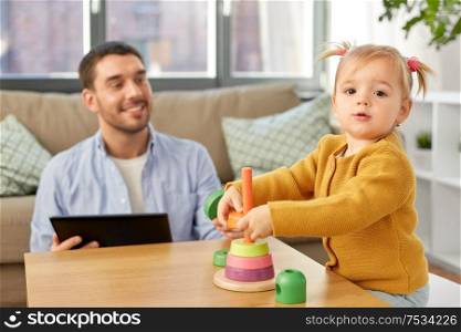 family, fatherhood and people concept - happy father with tablet pc computer and little baby daughter playing with pyramid toy at home. father with tablet pc and baby daughter at home