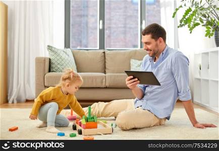 family, fatherhood and people concept - happy father with tablet pc computer and little baby daughter playing with wooden toy toy blocks kit at home. father with tablet pc and baby daughter at home