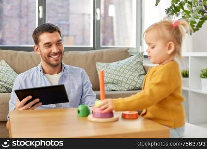 family, fatherhood and people concept - happy father with tablet pc computer and little baby daughter playing with pyramid toy at home. father with tablet pc and baby daughter at home