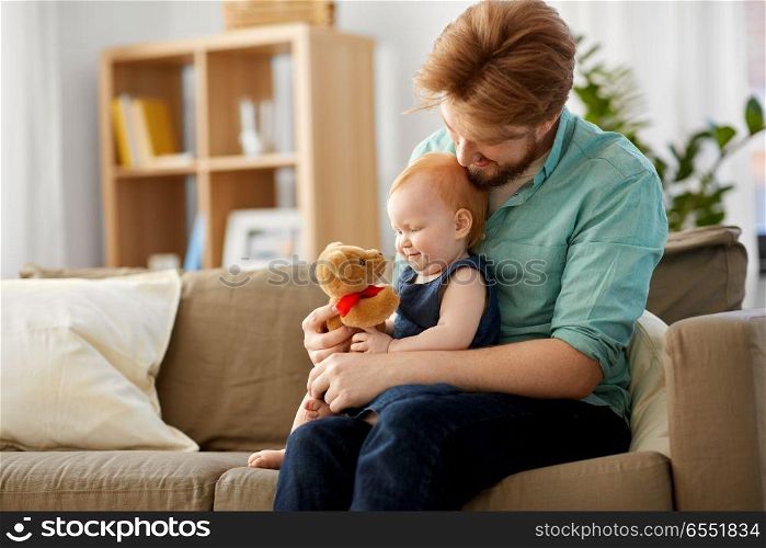 family, fatherhood and people concept - happy red haired father and little baby daughter playing with teddy bear at home. father and baby daughter with teddy bear at home. father and baby daughter with teddy bear at home