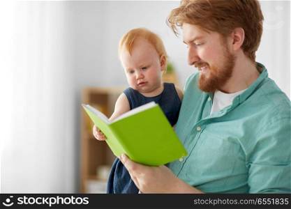 family, fatherhood and people concept - happy red haired father and little baby daughter with book at home. father and baby daughter with book at home. father and baby daughter with book at home