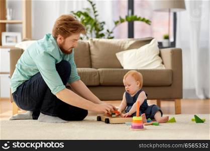 family, fatherhood and people concept - happy red haired father and little baby daughter playing with toy blocks kit at home. father and baby playing with toy blocks at home