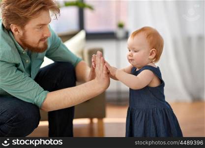 family, fatherhood and people concept - happy red haired father playing clapping game with little baby daughter at home. father with baby daughter playing clapping game. father with baby daughter playing clapping game