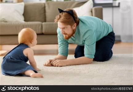 family, fatherhood and people concept - happy red haired father wearing cat ears headband playing with little baby daughter at home. father wearing cat ears headband playing with baby. father wearing cat ears headband playing with baby